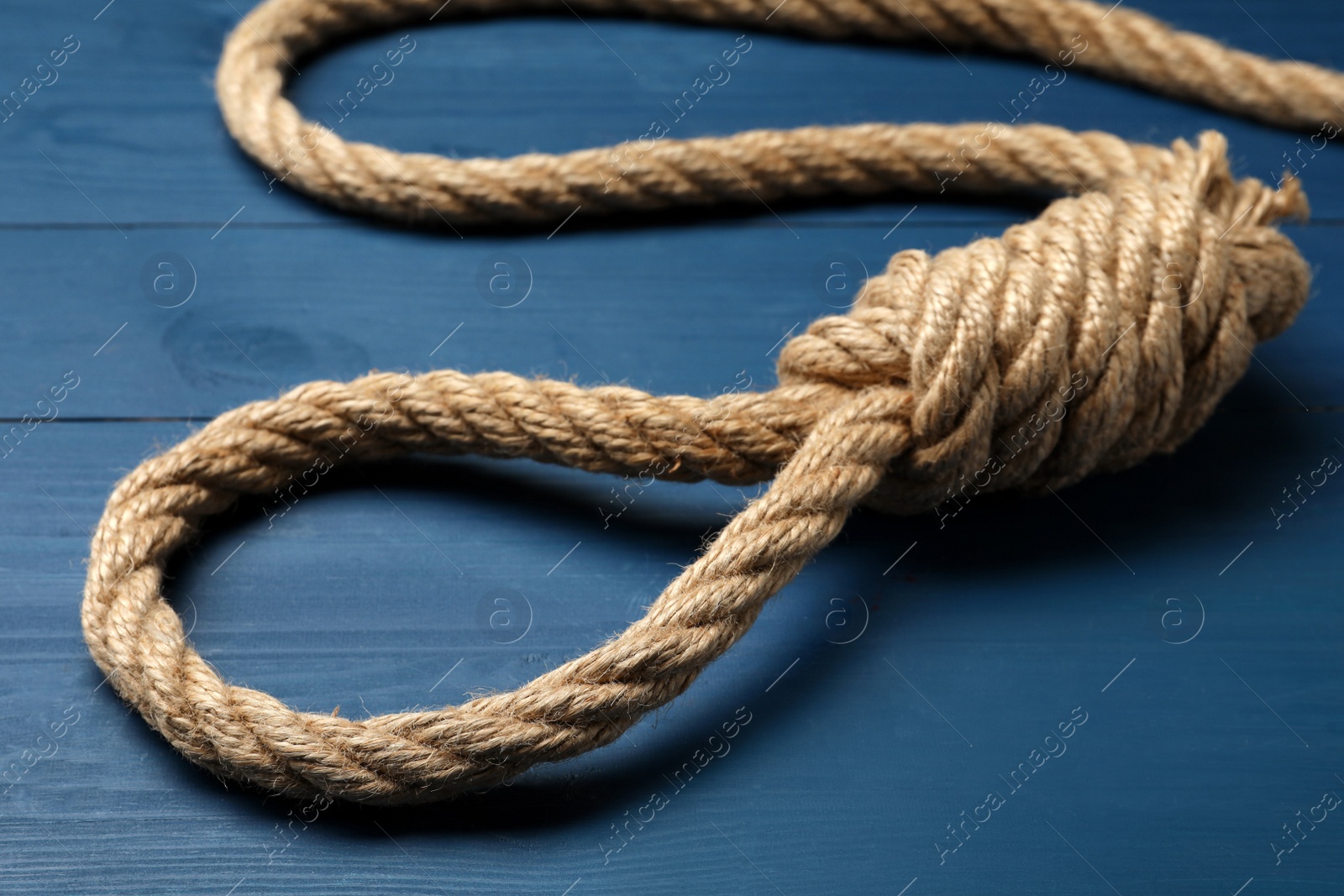 Photo of Rope noose with knot on blue wooden table, closeup