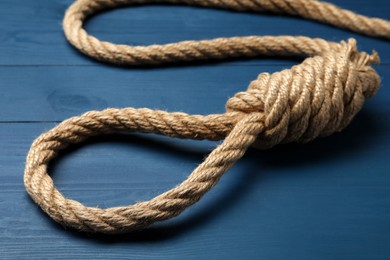 Rope noose with knot on blue wooden table, closeup