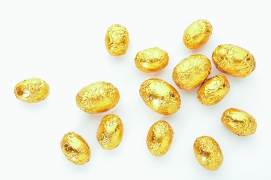 Photo of Many chocolate eggs wrapped in bright golden foil on white background, top view