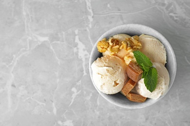 Bowl of delicious ice cream with caramel candies, popcorn and mint on light grey marble table, top view. Space for text