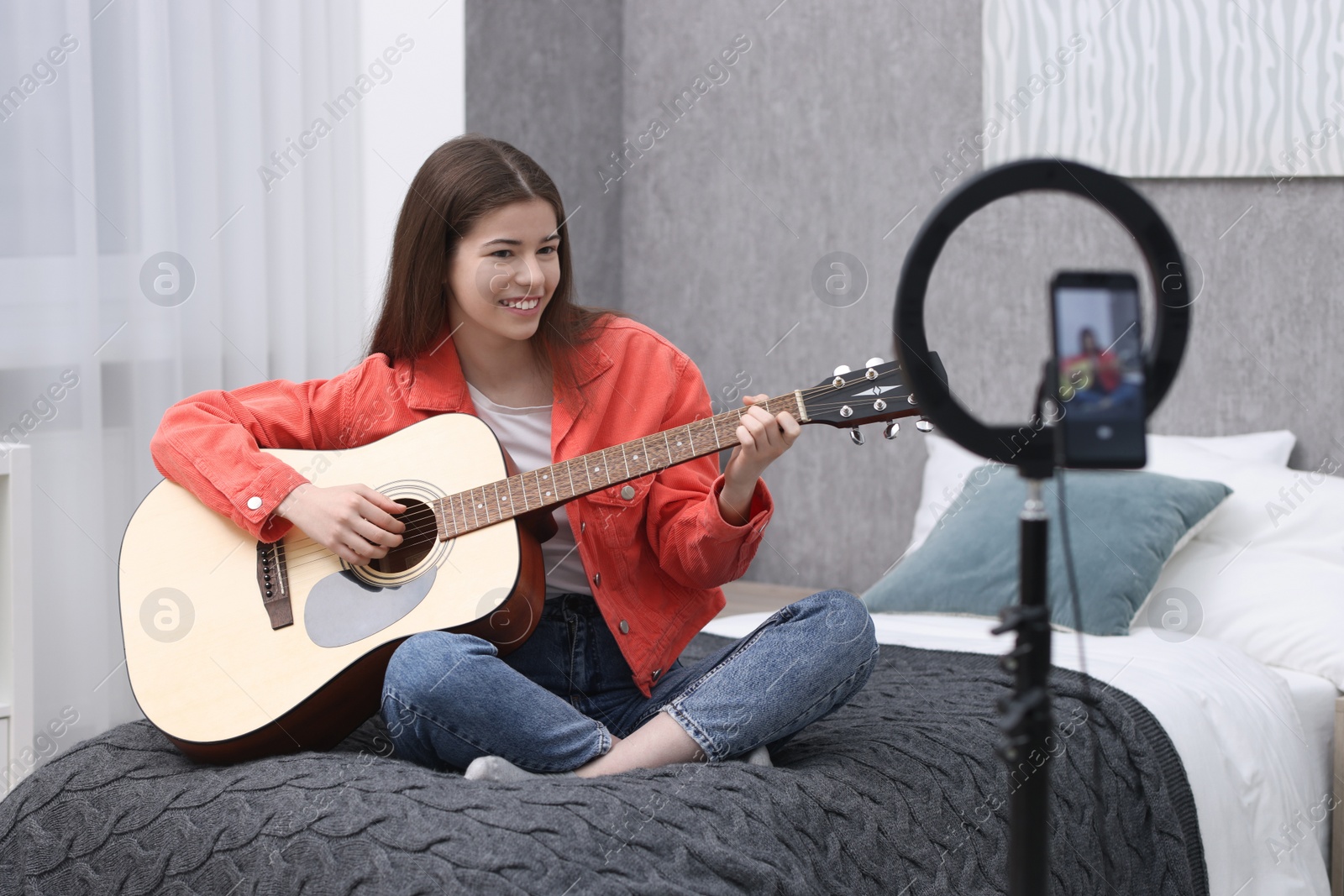 Photo of Smiling teenage blogger playing guitar while streaming at home