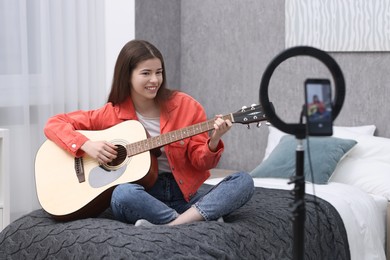 Photo of Smiling teenage blogger playing guitar while streaming at home