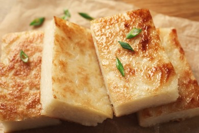 Photo of Delicious turnip cake with green onion on parchment paper, closeup