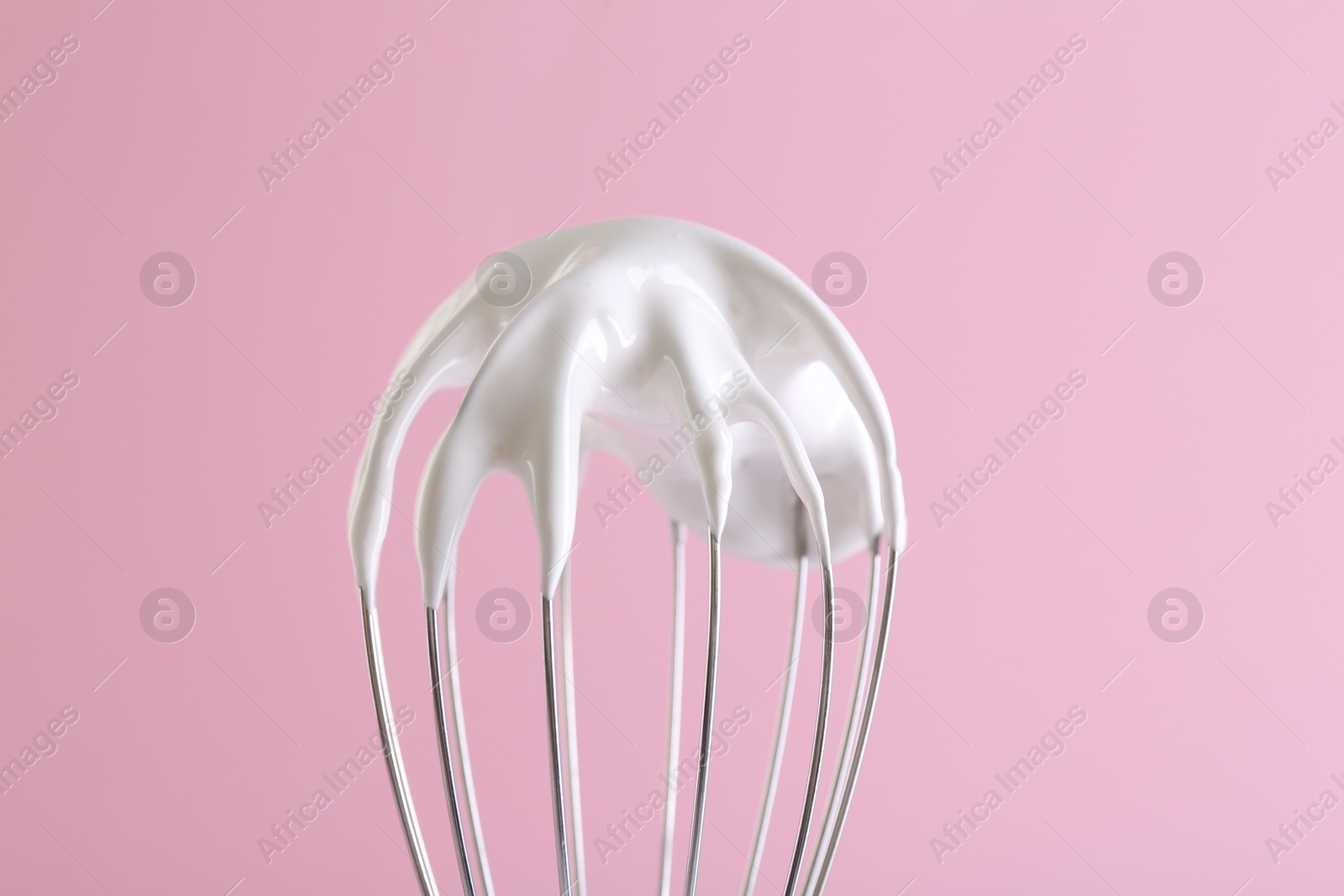 Photo of Whisk with whipped cream on pink background, closeup