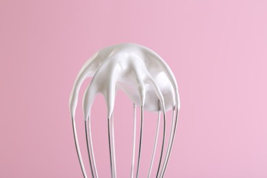 Whisk with whipped cream on pink background, closeup