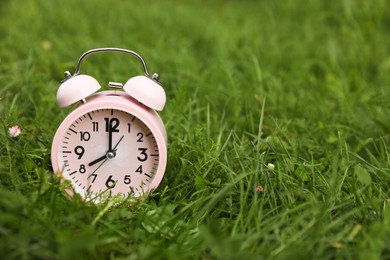 Photo of Pink alarm clock on green grass outdoors, space for text