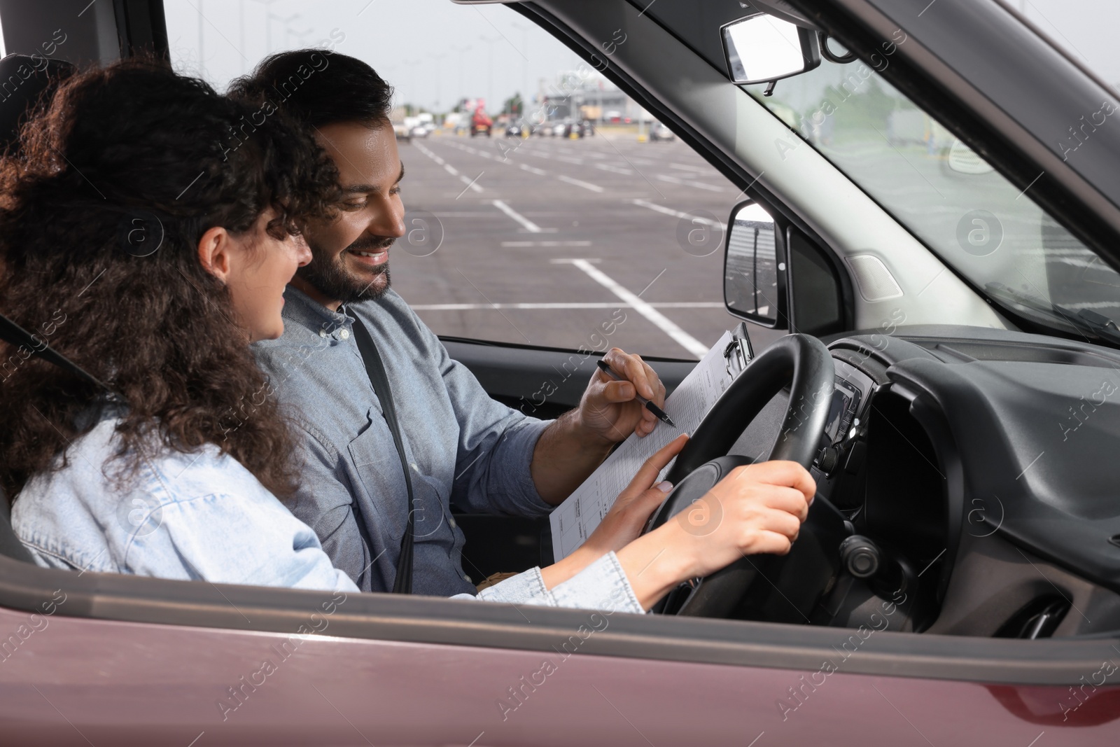 Photo of Driving school. Happy student passing driving test with examiner in car at parking lot