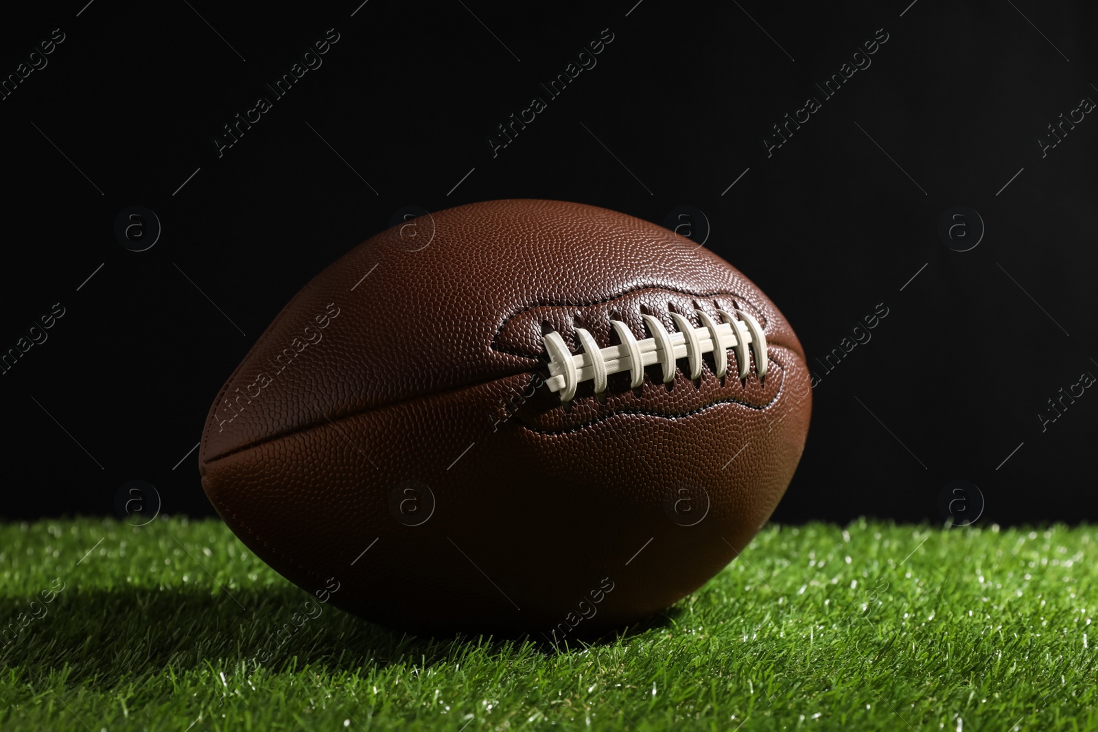 Photo of American football ball on green grass against black background