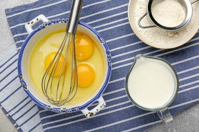 Photo of Whisk, eggs, milk and flour on grey table, flat lay