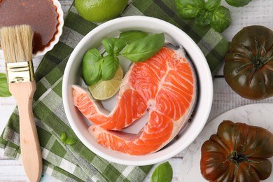 Photo of Fresh marinade, fish, brush, lime and other products on white wooden table, flat lay