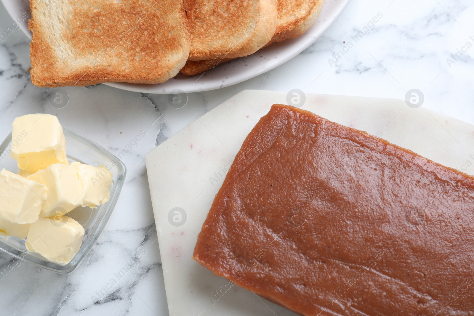 Photo of Quince paste with butter and toasts on white marble table, flat lay