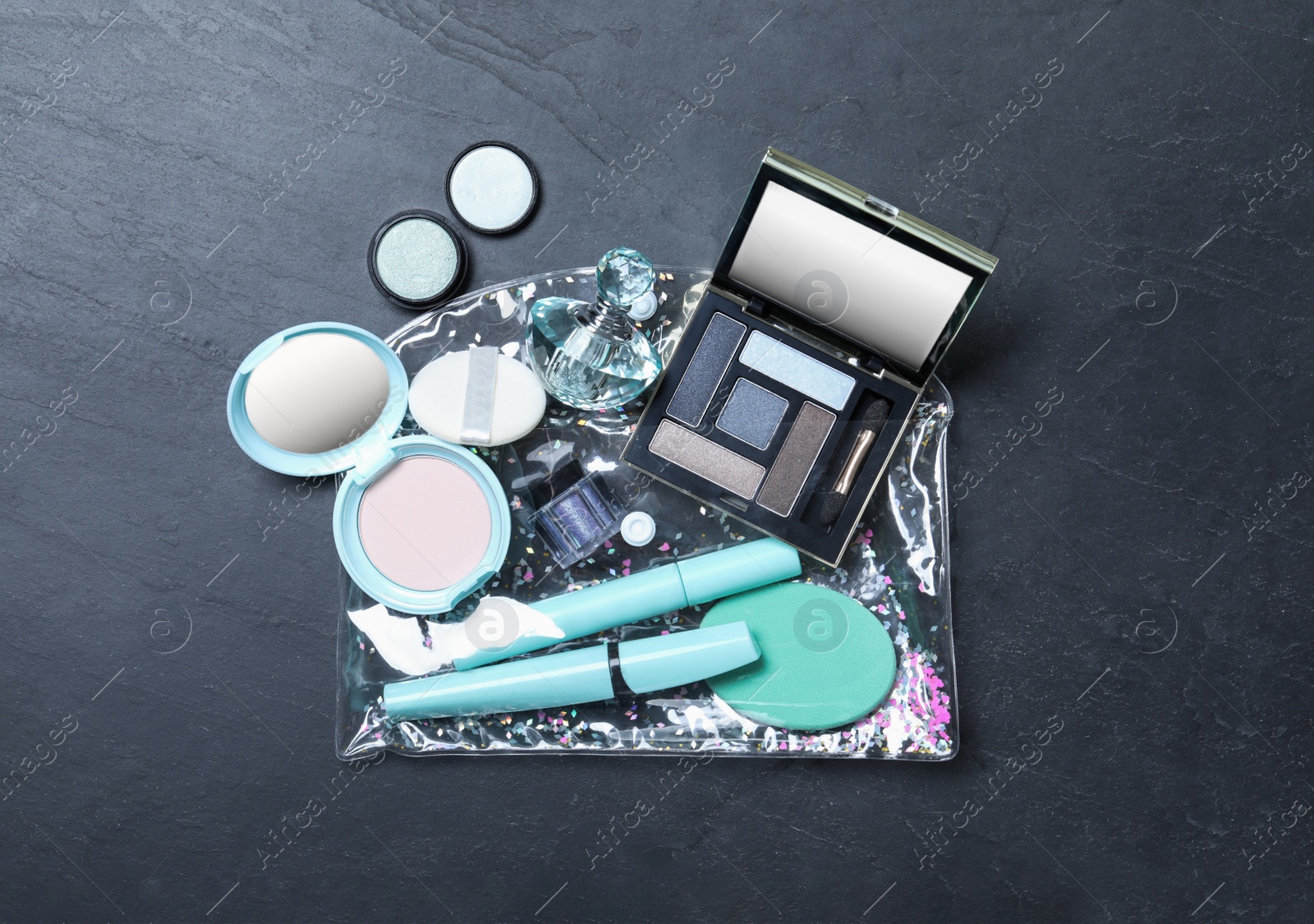 Photo of Cosmetic bag with makeup products and beauty accessories on black slate background, flat lay