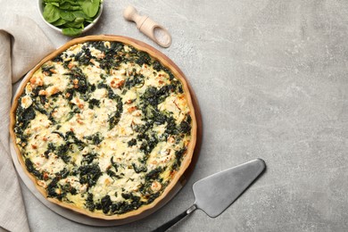 Delicious homemade quiche, fresh spinach leaves and spatula on light gray table, flat lay. Space for text