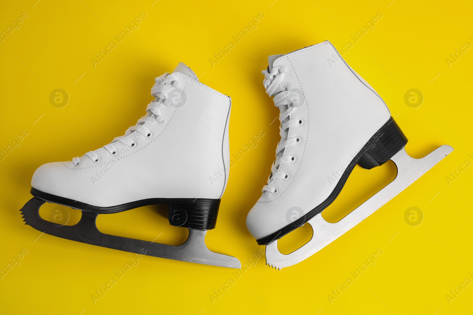 Photo of Pair of figure ice skates on yellow background, flat lay