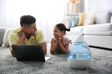 Photo of Father and daughter with laptop near modern air humidifier at home