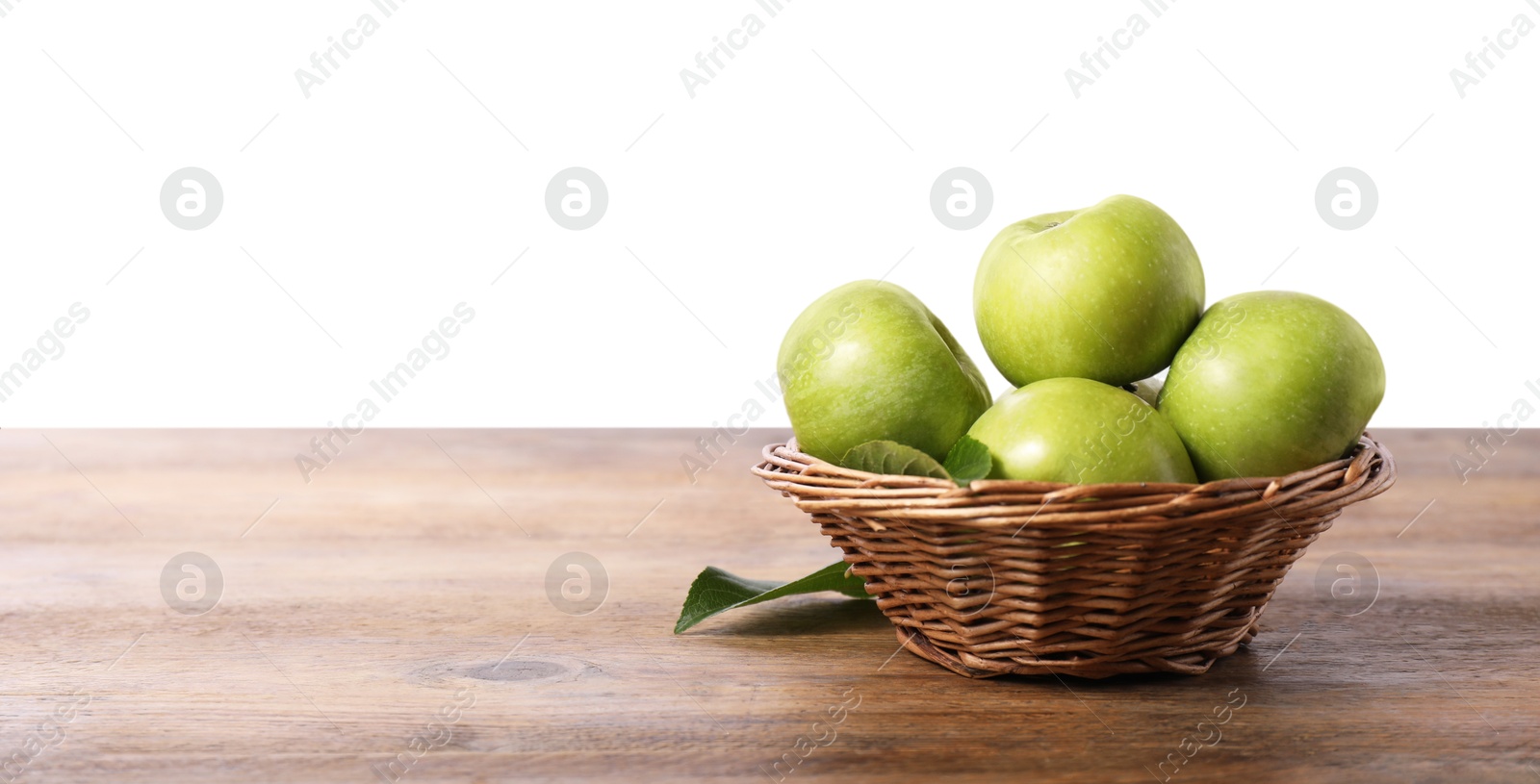 Photo of Ripe green apples in wicker basket on wooden table against white background. Space for text