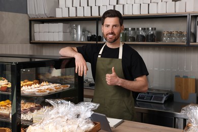 Happy seller showing thumb up at cashier desk in bakery shop