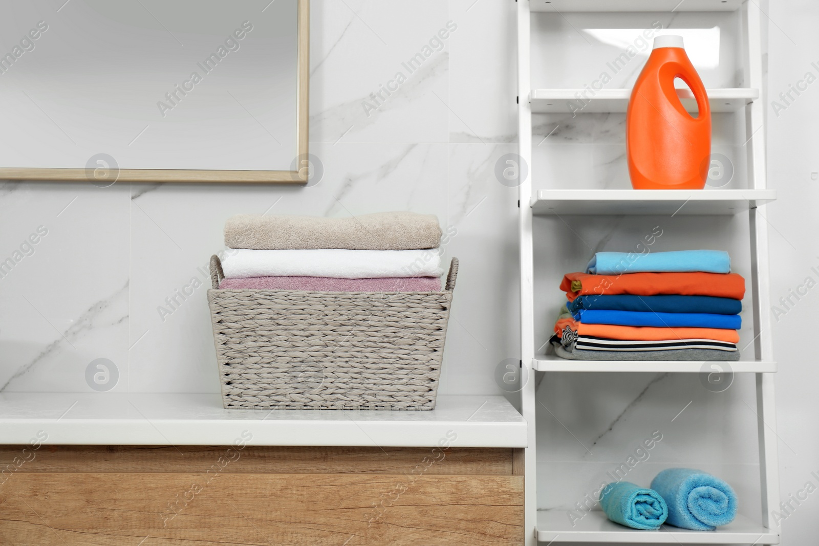 Photo of Fresh laundry and bottle of detergent in bathroom
