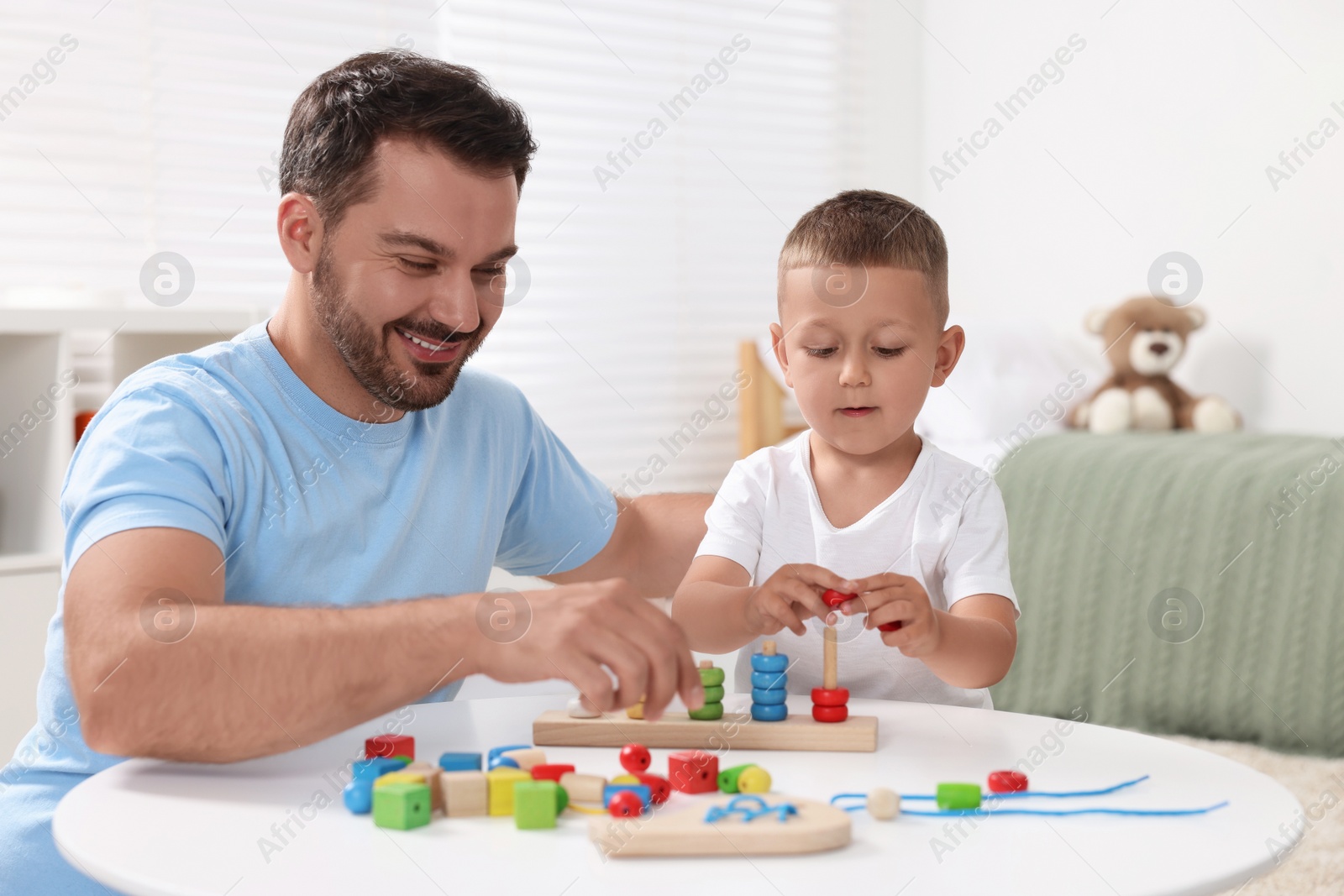 Photo of Motor skills development. Father and his son playing with stacking and counting game at table indoors