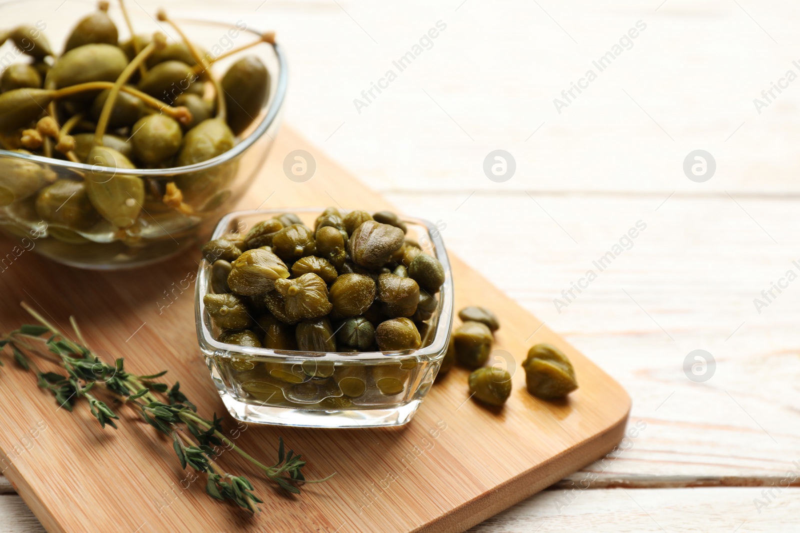 Photo of Tasty capers and thyme on white wooden table, space for text