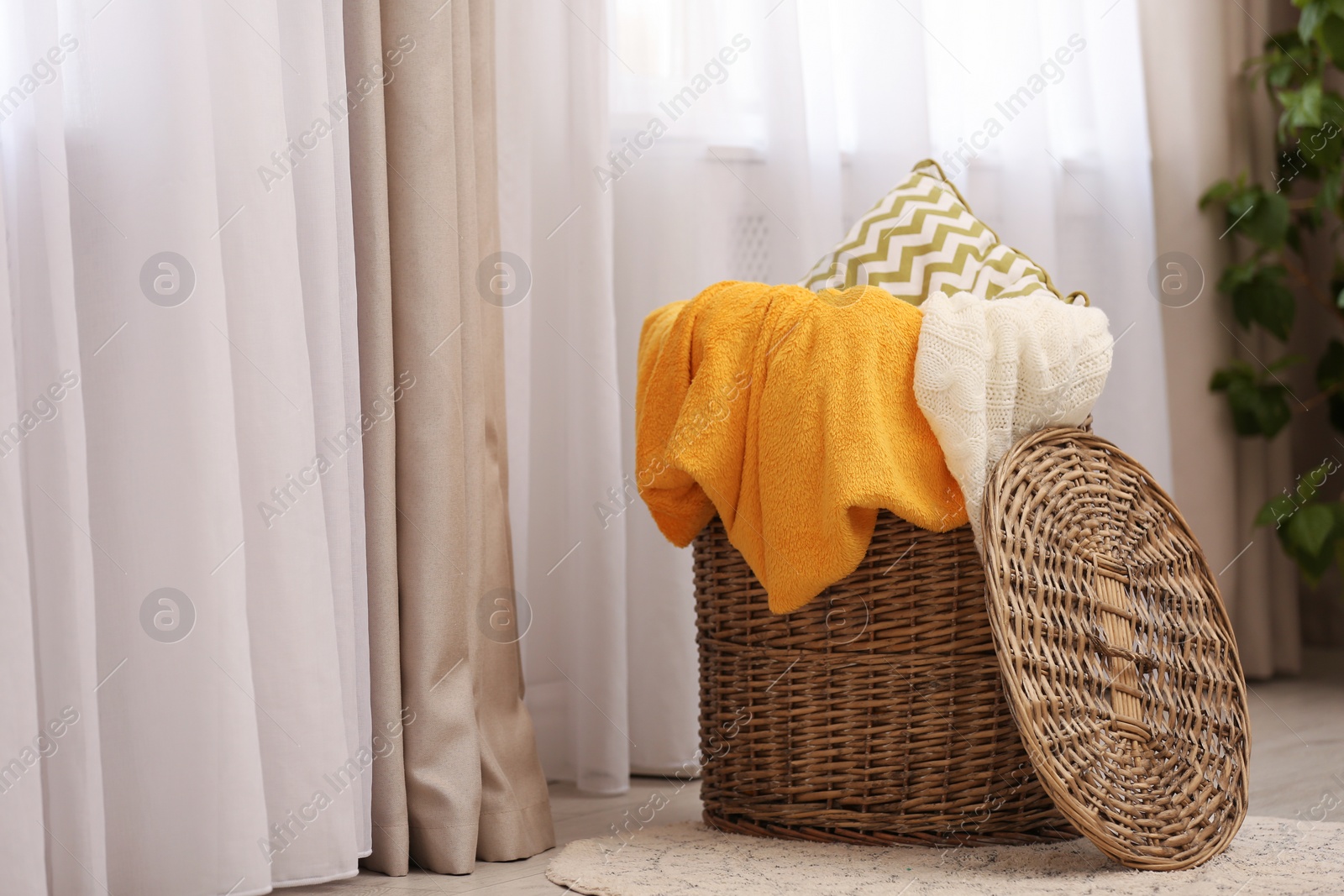 Photo of Basket with blankets and pillow near window indoors