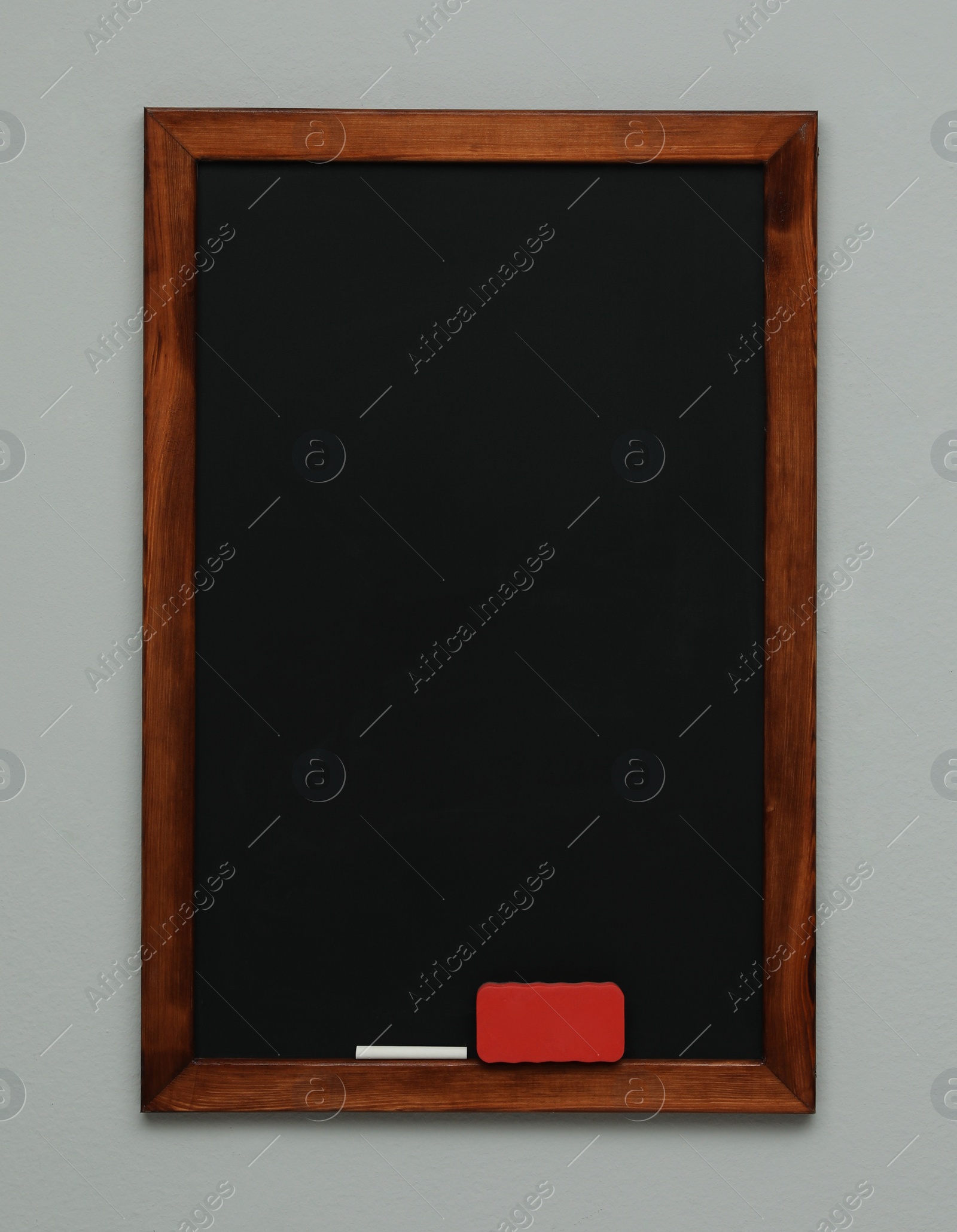 Photo of Clean blackboard with chalk and duster hanging on grey wall