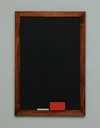 Photo of Clean blackboard with chalk and duster hanging on grey wall