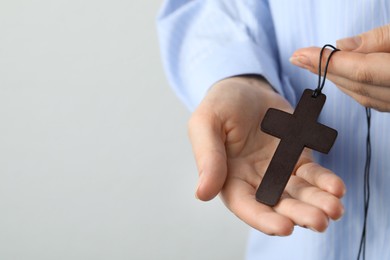 Photo of Woman holding wooden Christian cross on light grey background, closeup. Space for text