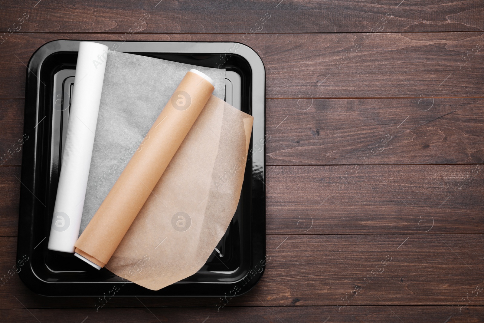 Photo of Rolls of parchment paper in baking pan on wooden table, top view. Space for text