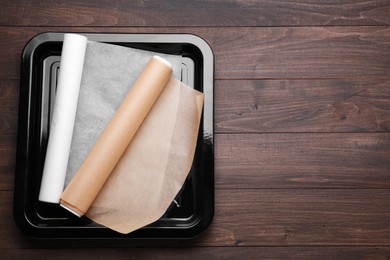 Photo of Rolls of parchment paper in baking pan on wooden table, top view. Space for text