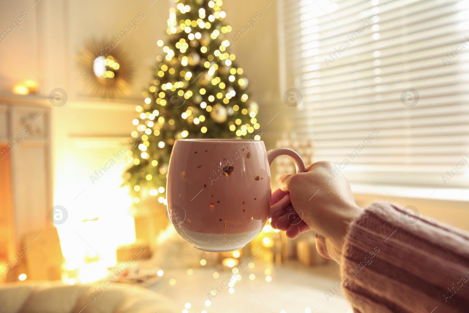 Photo of Woman with cup of drink and blurred Christmas tree on background, closeup