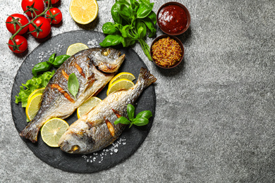 Photo of Delicious roasted fish with lemon on grey table, flat lay. Space for text