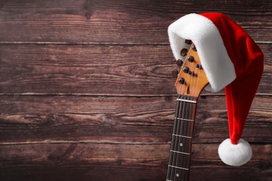 Guitar with cute Santa hat on wooden background, space for text. Christmas music
