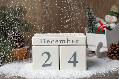 Photo of December 24 - Christmas Eve. Snow falling onto wooden block calendar and festive decor on table