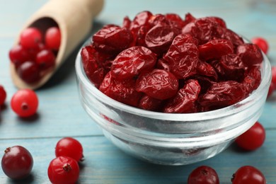 Tasty dried cranberries in bowl and fresh ones on light blue wooden table, closeup