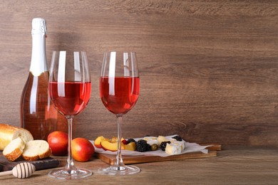Photo of Delicious rose wine and snacks on wooden table, space for text