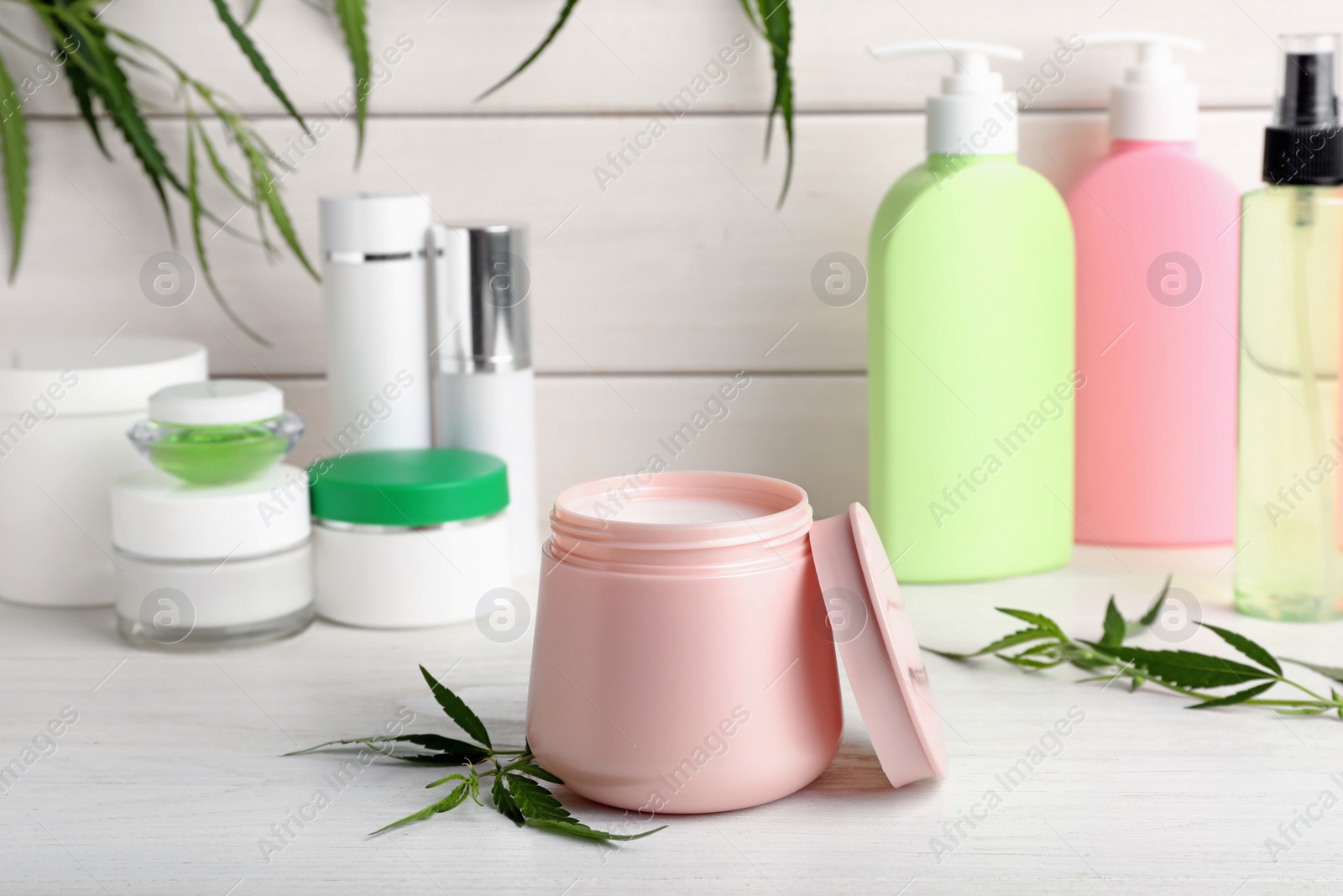 Photo of Hemp cosmetics and green leaves on white wooden table