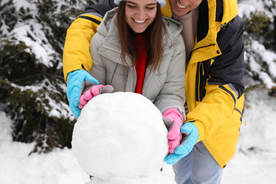 Photo of Happy couple making snowman outdoors, closeup. Winter vacation