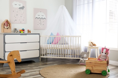 Photo of Baby room interior with cute posters, chest of drawers and comfortable crib