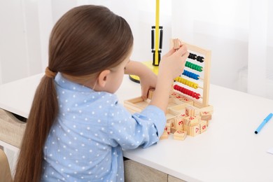 Cute little girl playing with wooden cubes at desk in room. Home workplace