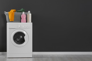 Photo of Washing machine with clothes and detergents near black wall indoors, space for text. Interior design