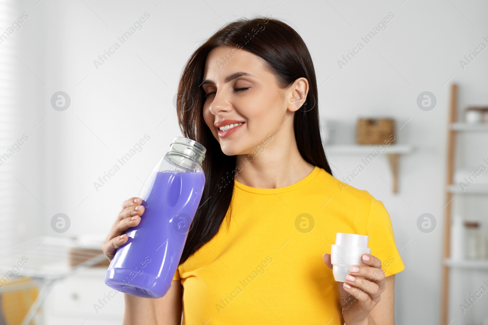 Photo of Beautiful woman smelling fabric softener in bathroom