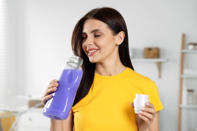 Beautiful woman smelling fabric softener in bathroom