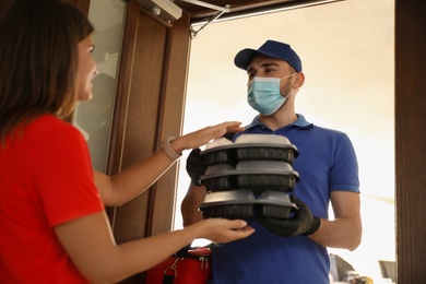Courier in protective mask and gloves giving order to woman at entrance. Restaurant delivery service during coronavirus quarantine