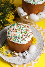 Traditional Easter cakes with sprinkles, painted eggs and beautiful spring flowers on yellow background