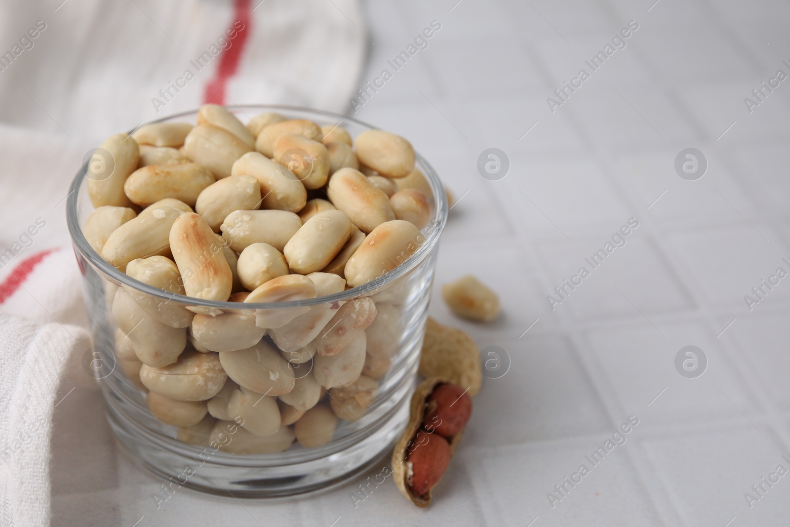 Photo of Roasted peanuts in bowl on white tiled table, closeup. Space for text