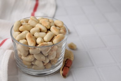 Photo of Roasted peanuts in bowl on white tiled table, closeup. Space for text