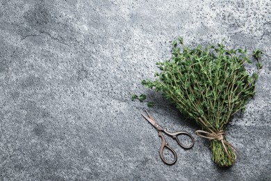 Photo of Bunch of aromatic thyme and scissors on grey table, flat lay. Space for text