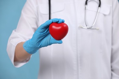 Doctor holding red heart on light blue background, closeup