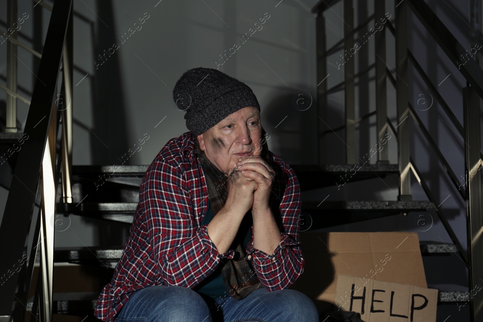 Photo of Poor senior man with cardboard sign HELP on stairs indoors